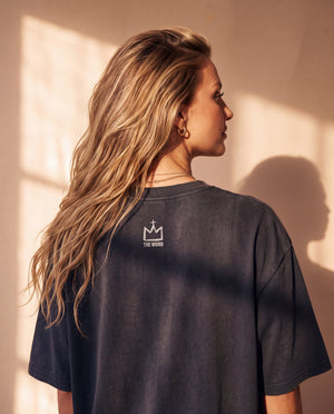 Jesus Is King faded black tee, back view of a woman with long wavy hair over one shoulder, small crown logo under the neckline