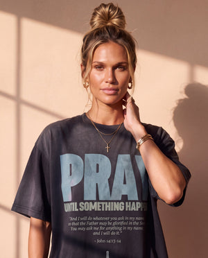 Pray Until Something Happens faded black tee, close up portrait of a woman with a hair bun and cross necklace above the PRAY lettering