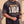 Heart of a Lion faded black tee, front print, man lifting the hem with both hands, distressed HEART OF A LION lettering in view