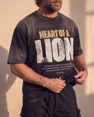 Heart of a Lion faded black tee, front print, man lifting the hem with both hands, distressed HEART OF A LION lettering in view
