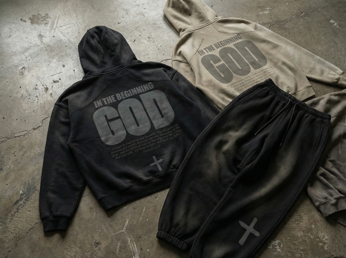Faded black and sand IN THE BEGINNING GOD hoodies and sweatpants laid on concrete - The Word