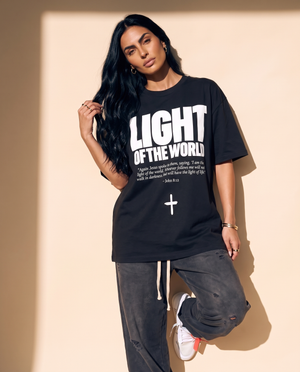 Light of the World tee, black, front print, woman, leaning on wall full body