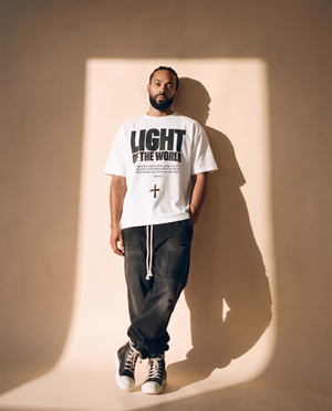 Light of the World tee, white, front print, man, leaning on wall full body