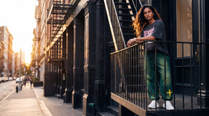Woman in the mineral green heavyweight sweatpants on a SoHo fire escape, The Word