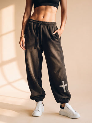 Woman wearing the smoky black heavyweight sweatpants in slow motion, close on the cross at the ankle, the crown logo on the back pocket and full length from the front