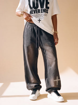 Woman wearing the dark grey heavyweight sweatpants with a white Love Never Ends tee in slow motion, close on the cross at the ankle, the crown logo on the back pocket and full length from the front