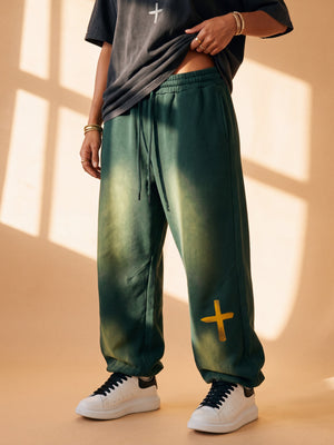 Woman wearing the mineral green heavyweight sweatpants with a black Daughter of the King tee in slow motion, close on the gold cross at the ankle, the crown logo on the back pocket and full length from the front