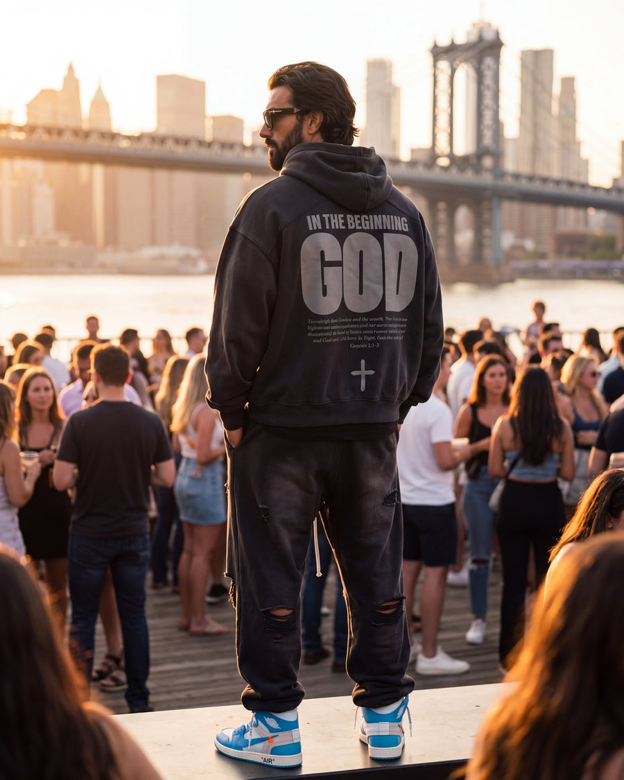 A man in The Word In the Beginning God hoodie, back print, facing the Manhattan Bridge at sunset