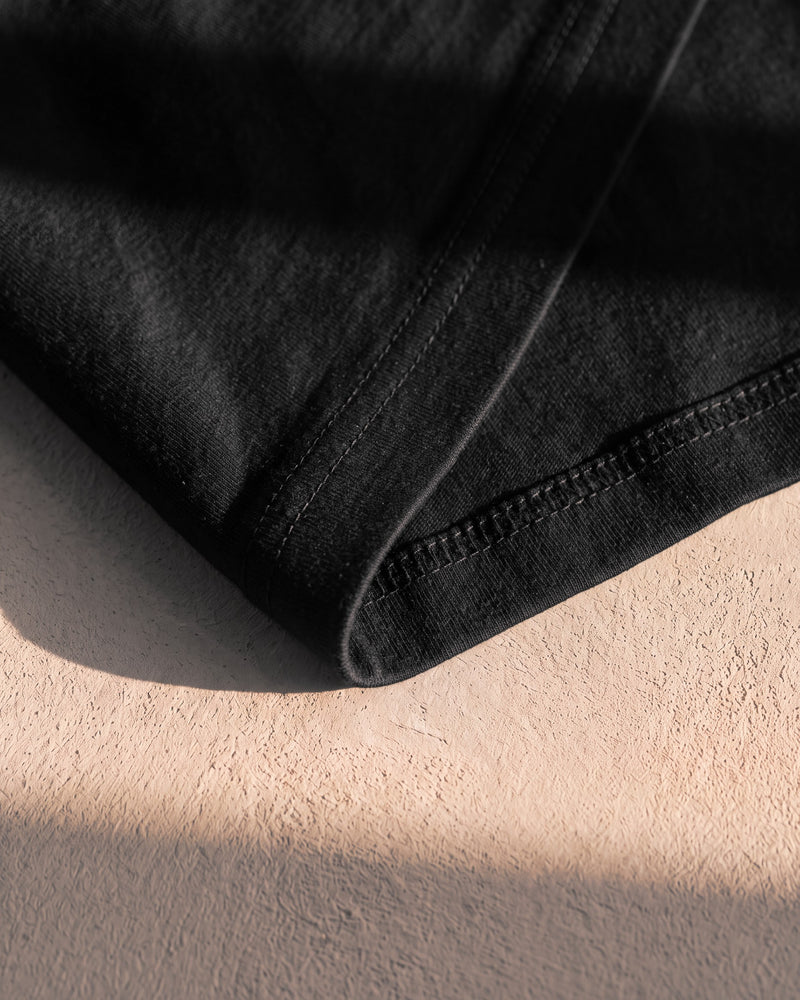 Coverstitch hem on a black 240 gsm The Word tee in warm sunlight