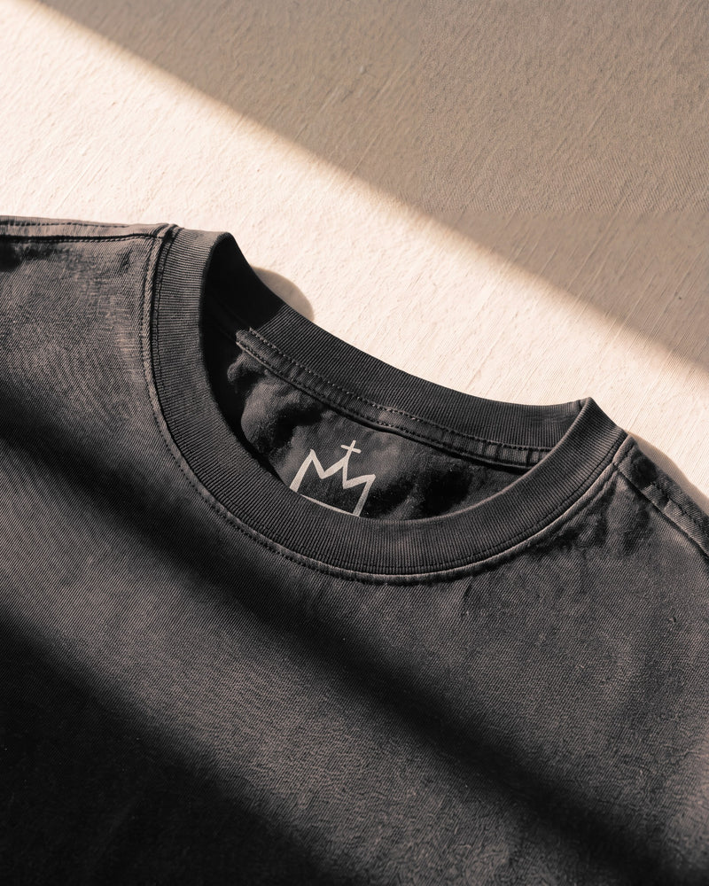 Double-stitched ribbed collar with the crown neck logo behind it on a faded black The Word tee