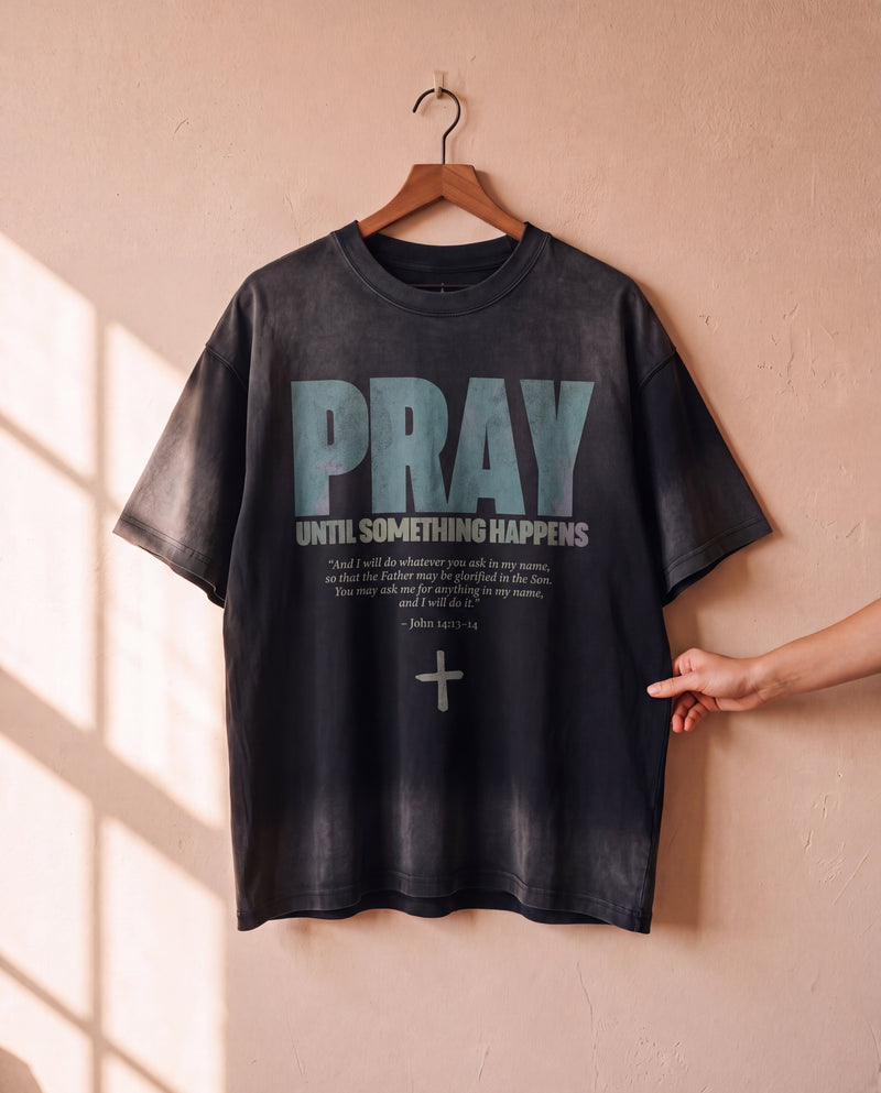 Pray Until Something Happens faded black tee on a hanger, front print